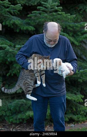 Homme âgé tenant le chat et le chien jouet Bolonka Zwetna pup dans ses bras, Allemagne Banque D'Images