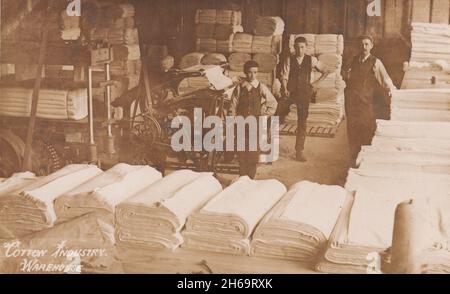 Entrepôt de l'industrie du coton, Bury, Lancashire: Des morceaux de tissu sont au premier plan, un homme et deux garçons sont posés derrière eux (les hommes ont vérifié le tissu pour des défauts avant expédition) Banque D'Images