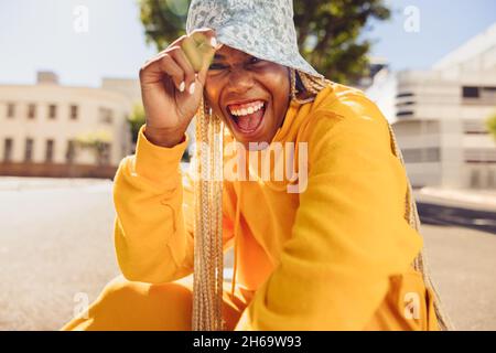 Une jeune femme insouciante s'amuse au soleil.Une jeune femme heureuse souriant à l'appareil photo tout en étant assise à l'extérieur pendant une journée d'été.Vêtements de jeune femme vibrants Banque D'Images