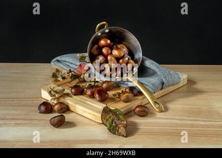 Encore la vie avec la casserole de châtaignier rôtie sur table de bambou et tissu gris Banque D'Images