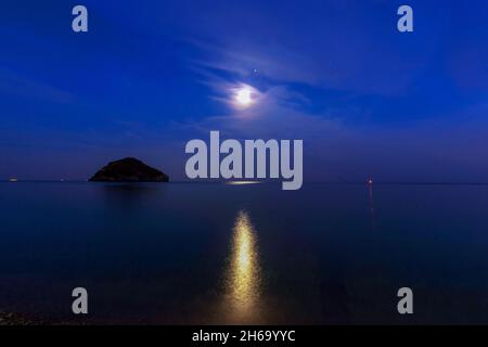 Pleine lune se reflétant dans l'eau bleue de la mer formant un magnifique rayon de lumière jaune qui s'étend le long d'une île Banque D'Images