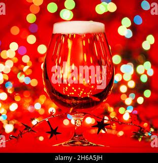 Plein verre de bière de lager ou de pilsner avec guirlande de Noël et lumières sur fond rouge Banque D'Images