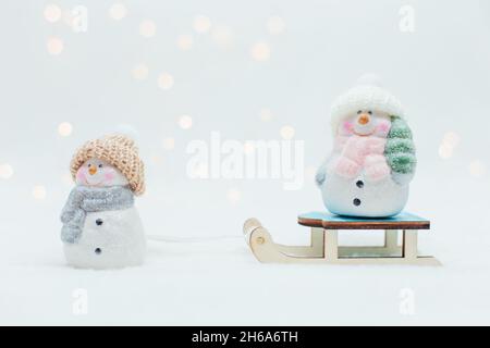 Figurines décoratives sur le thème de Noël.Deux statuettes d'un bonhomme de neige dans un chapeau tricoté sur le traîneau.Décoration festive, lumières bokeh chaleureuses Banque D'Images