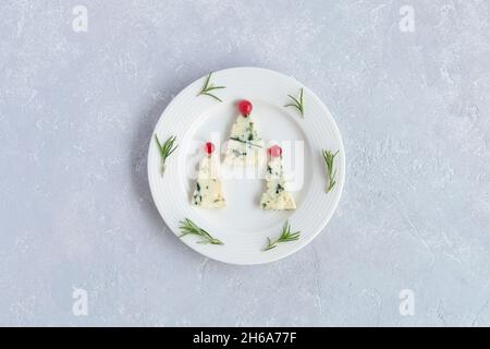 arbres du nouvel an fabriqués au fromage roquefort et décorés de raisins de corinthe rouges, sur une assiette, fond gris, vue de dessus Banque D'Images