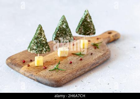 Hors-d'œuvre d'arbres de Noël en fromage doux sur une planche à découper sur fond blanc, gros plan, vue latérale Banque D'Images