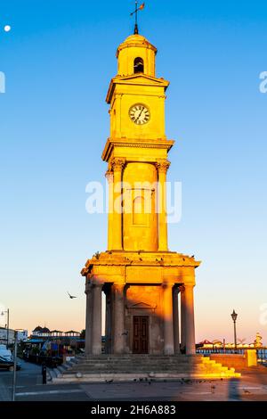 La tour de l'horloge sur le front de mer déserté de la station balnéaire de Herne Bay.Tour revêtue de pierre en début de matinée, à l'heure d'or, contre un ciel bleu clair. Banque D'Images