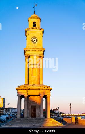 La tour de l'horloge sur le front de mer déserté de la station balnéaire de Herne Bay.Tour revêtue de pierre en début de matinée, à l'heure d'or, contre un ciel bleu clair. Banque D'Images