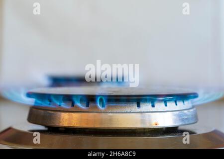 Anneau à gaz allumé sur la table de cuisson à gaz.Anneau circulaire gris recouvert d'un dessus noir en fonte, flammes bleues provenant des évents à gaz sur le côté de l'anneau. Banque D'Images