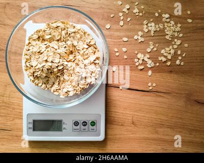 Gruaux d'avoine, gruaux pesant dans un bol en verre sur des balances électroniques de cuisine sur une table en bois. Banque D'Images