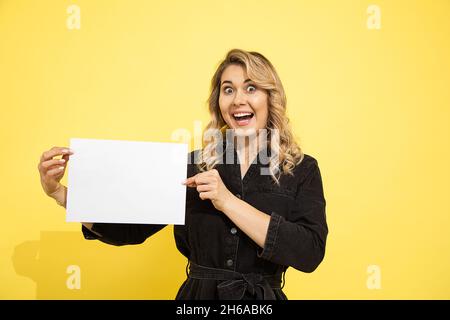 Photo de jeune jolie femme blonde rit joyeusement sur fond jaune, prise en studio, garde vide vide pour les inscriptions Banque D'Images