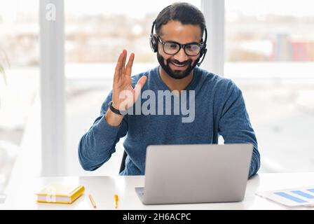 Un employé indien sympathique portant un casque et des lunettes de vue en ligne, tenant un appel vidéo, participer à une réunion virtuelle, hommes multiraciaux en tenue décontractée parlant en ligne Banque D'Images