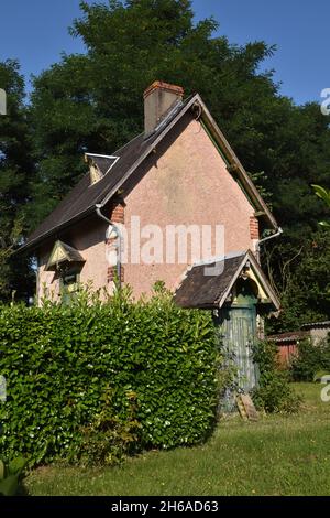 Un charmant petit bâtiment, un abri de jardin glorifié, avec un toit en ardoise à pente raide avec une cheminée et de minuscules fenêtres à pignons, peint rose foncé, Banque D'Images