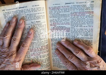 Ma mère/grand-mère de 94 ans, lit dans sa Bible Jean 3:16. Vieux script allemand.Le concept des enseignements de Jésus. Banque D'Images