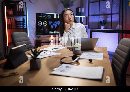 Femme d'affaires asiatique attentionnés, assise au bureau avec un ordinateur portable moderne et vue de côté.Femme membre de l'entreprise à la recherche de nouvelles idées dans les affaires. Banque D'Images
