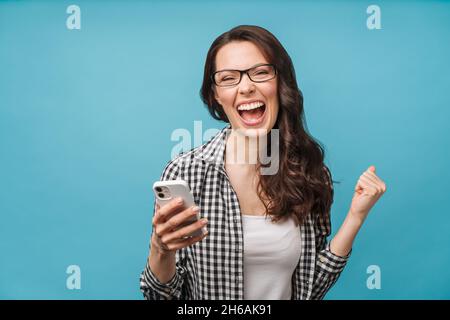 Joyeux brunette excité regardant l'écran du téléphone, célébrant la victoire en ligne, surjoyeuse jeune femme criant avec joie, tenant le smartphone, lisant bien Banque D'Images