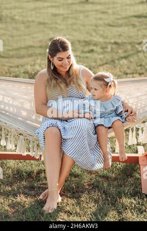 Charmante femme enceinte en été, la sundress se repose avec sa petite fille dans un hamac dans la nature, enfant de 3 ans.Matériaux naturels.Joyeux Banque D'Images