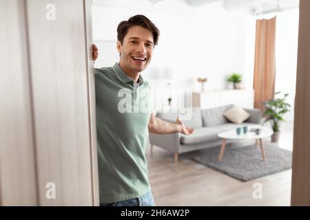 Bienvenue.Portrait d'homme joyeux invitant le visiteur à entrer dans sa maison, jeune garçon heureux debout dans la porte de l'appartement moderne, tenue millénaire Banque D'Images