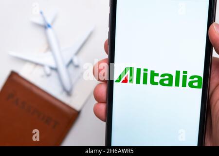 L'application Alitalia Airline sur l'écran du smartphone est disponible.Un avion de jouet blanc et un passeport sont posés sur une table avec une surface légère.novembre 2021, San Francisco, Etats-Unis Banque D'Images