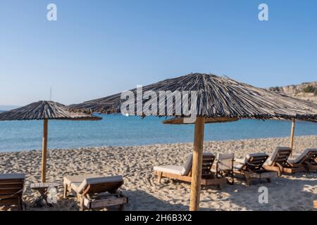 Vacances d'été en bord de mer.Parasols en paille chaises longues en rangée sur la plage de sable vide par beau temps.Relaxation sur des chaises en bois sous des parasols, Elafonissos isl Banque D'Images