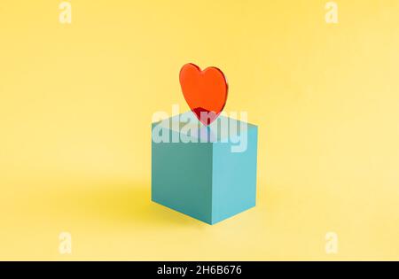 Un coeur rouge sur un cube bleu isolé sur un fond jaune.Saint Valentin.Disposition rectangulaire avec espace de copie.Concept abstrait.Isométrique. Banque D'Images