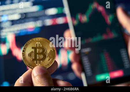 Trader investisseur tenant le téléphone et la pièce d'achat bitcoin sur le marché de crypto. Banque D'Images