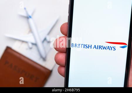 Logo de la compagnie British Airways sur l'écran du téléphone portable dans la main de l'homme sur le fond du passeport, carte d'embarquement et avion, septembre 2021, San Francisco, USA. Banque D'Images