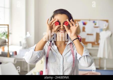 Portrait drôle de la femme heureuse qui travaille comme couturière couvrant ses yeux avec deux boutons Banque D'Images