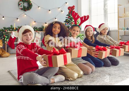Les enfants de 8-9 ans s'assoient dans une rangée et tiennent leurs cadeaux de Noël devant eux. Banque D'Images