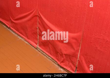 Vieux papier peint rouge qui se détache du mur.Décollement du vieux papier.La nécessité de réparer, de reconstruire et de recoller le papier peint. Banque D'Images