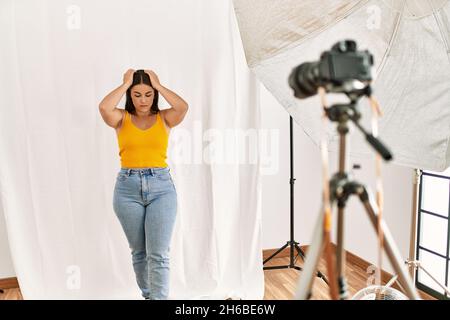 Jeune belle femme hispanique posant comme modèle au studio de photographie souffrant de maux de tête désespérés et stressés parce que la douleur et la migraine. Mains o Banque D'Images