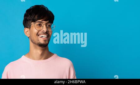 Gros plan portrait d'un homme indien à barbe gai avec des lunettes qui se posent sur un arrière-plan de studio bleu, regardant l'espace de copie, panorama.Beau jeune homme moi Banque D'Images