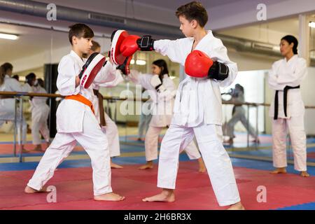 Deux garçons en gants de boxe lançant des coups pendant l'entraînement d'auto-défense dans la salle de gym Banque D'Images