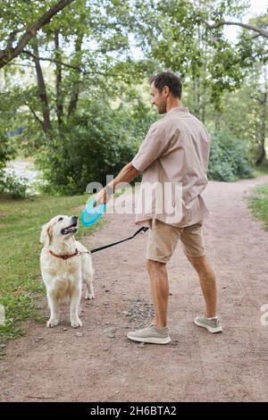 Portrait vertical complet d'un homme souriant jouant avec un chien à l'extérieur en été dans un parc verdoyant Banque D'Images