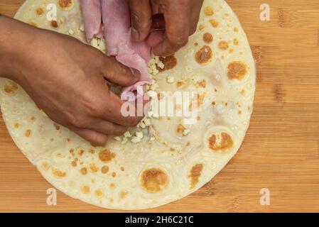 Le chef plaçant le jambon cuit avec ses mains sur du fromage frais haché à l'intérieur d'une crêpe salée Banque D'Images