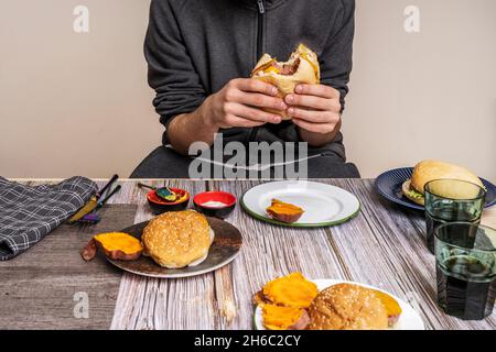 jeune personne mangeant des hamburgers de boeuf avec sauces, patate douce cuite et des verres de soda sur une table en bois Banque D'Images