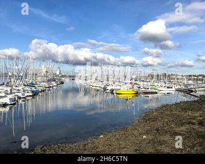 Dans un ciel bleu intense, des nuages en torsion dansent sur les eaux claires et remplies de bateaux de Port-Louis dans le sud du Morbihan, en Bretagne, en France. Banque D'Images