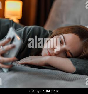 Triste adolescente souffrant d'insomnie surfant sur Internet ou bavardant avec un smartphone la nuit couché sur le lit. Dépression dépendance d'Internet. Jeune Banque D'Images