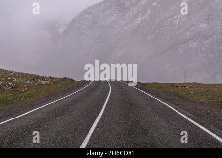 Vue d'automne pittoresque avec route asphaltée dans les montagnes pendant les fortes chutes de neige Banque D'Images