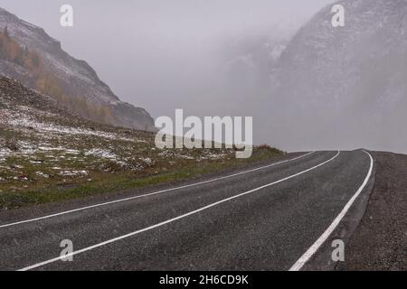 Vue d'automne pittoresque avec route asphaltée dans les montagnes pendant les fortes chutes de neige Banque D'Images