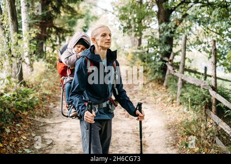 Un enfant endormi et fatigué marchant avec son père dans un sac à dos dans les montagnes.Marche nordique avec la famille et l'enfant à l'automne. Obstacles et défis pour l'homme Banque D'Images