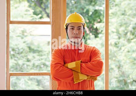 Portrait de jeunes contremaître vietnamiens debout avec les bras croisés devant de grandes fenêtres fraîchement installées Banque D'Images