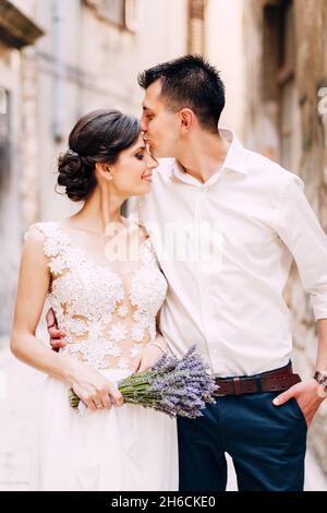 Sibenik, Croatie - 05.06.17: Marié câlins et baisers mariée dans un front dans une robe de dentelle blanche avec un bouquet de lavande dans ses mains sur la rue de Banque D'Images