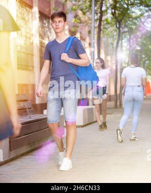 Adolescent marchant dans la rue, portant un sac sur une épaule Banque D'Images