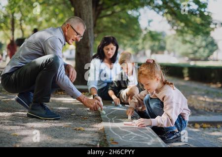 Couple senior avec petits-enfants tirant avec des craies sur la chaussée à l'extérieur dans le parc. Banque D'Images