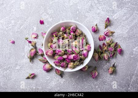 Vue de dessus d'un bol blanc avec boutons de rose séchés pour le thé parfumé sur fond de béton gris Banque D'Images