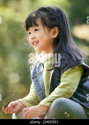 portrait extérieur d'une petite fille asiatique assise sur l'herbe heureuse et souriante Banque D'Images