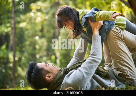 père asiatique et fille s'amusant dehors sur l'herbe dans le parc de la ville Banque D'Images