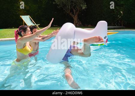 Deux amis qui jettent un homme d'une licorne arc-en-ciel flottent dans la piscine. Banque D'Images