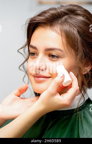 Maquilleuse appliquant le tube de la fondation de la crème rouilleuse sur la joue de la jeune femme caucasienne dans un salon de beauté Banque D'Images