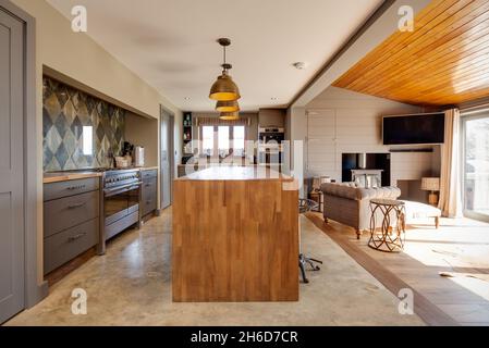 Suffolk, Angleterre - Mars 2018: Maison cuisine intérieure salle familiale montrant le bar petit déjeuner avec tabourets et coin salon devant un poêle à bois. Banque D'Images